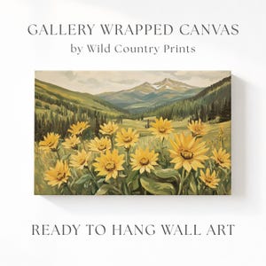 Puede incluir: Un lienzo envuelto en galería de Wild Country Prints que presenta una pintura de paisaje con flores silvestres amarillas en primer plano, colinas verdes y una cordillera nevada al fondo bajo un cielo pálido.