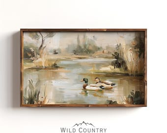 May include: A framed landscape painting depicts two ducks swimming in a pond. The artwork features a muted color palette of greens, browns, and beige, with a wooden frame. The painting is signed "Wild Country Collective".