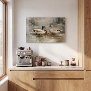 a kitchen counter with a coffee machine, coffee cups, and a painting of ducks swimming in a pond.