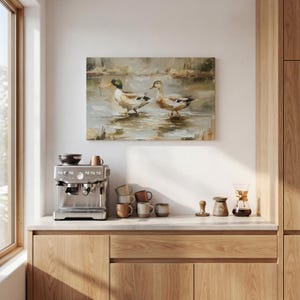 a kitchen counter with a coffee machine, coffee cups, and a painting of ducks in a pond.