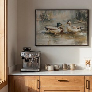 a kitchen counter with a coffee maker, coffee cups, and a framed painting of ducks swimming in a pond.