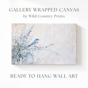May include: A gallery wrapped canvas wall art piece by Wild Country Prints featuring a light blue bird perched on thin, delicate branches against a soft, neutral cream and beige background. The artwork is ready to hang and displays a bird.