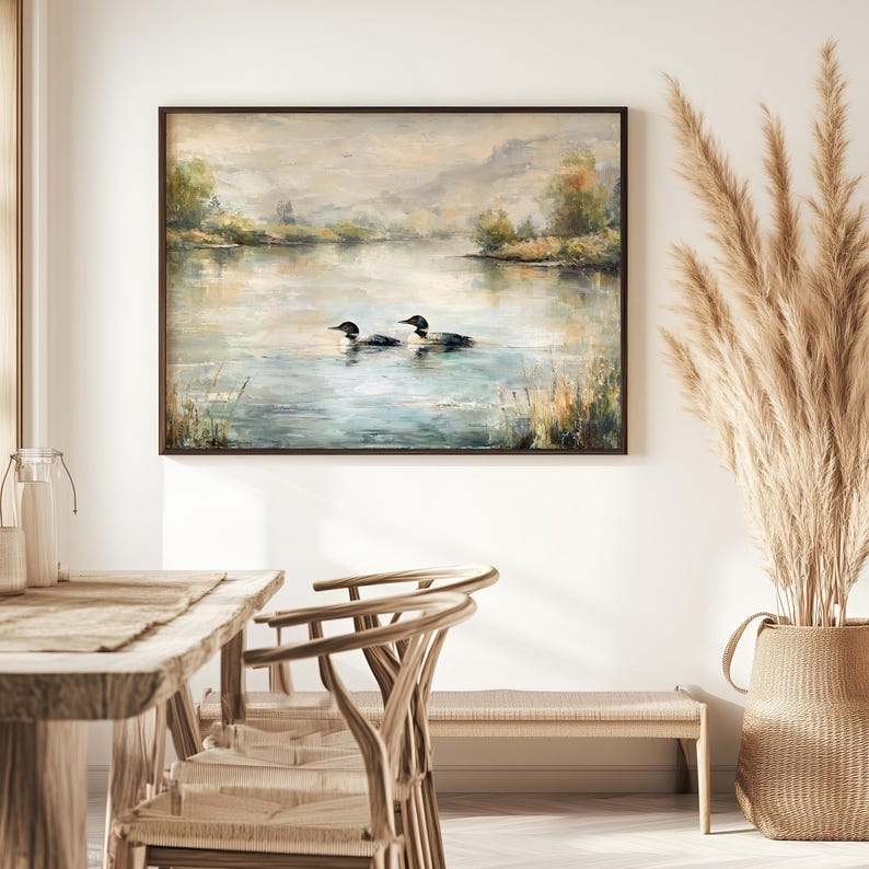 a serene indoor setting with a painting of ducks swimming in a lake hanging on the wall above a wooden dining table and chairs.
