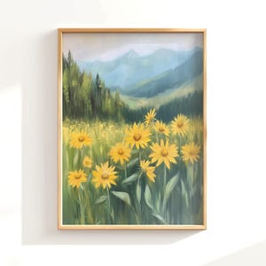 Puede incluir: Pintura de paisaje enmarcada que representa un campo de flores amarillas en primer plano, con un bosque y montañas al fondo. La obra de arte está en un marco dorado y tiene un estilo suave y pictórico.