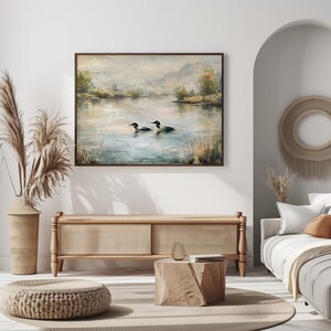 a serene living room with a large painting of ducks swimming on a lake hanging on the wall. The room is decorated with a beige sofa, a wooden coffee table, and a woven ottoman. The overall color scheme and arrangement of the furniture and artwork create a calm and inviting atmosphere.