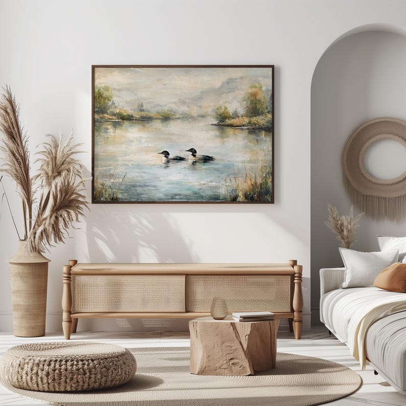 a serene living room with a large painting of ducks swimming on a lake hanging on the wall. The room is decorated with a beige sofa, a wooden coffee table, and a woven ottoman. The overall color scheme and arrangement of the furniture and artwork create a calm and inviting atmosphere.