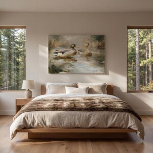 a serene bedroom scene with a large bed, a painting of ducks in a pond, and two windows overlooking a forest.