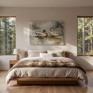 a serene bedroom scene with a large bed, a painting of ducks on the wall, and two windows overlooking a forest.