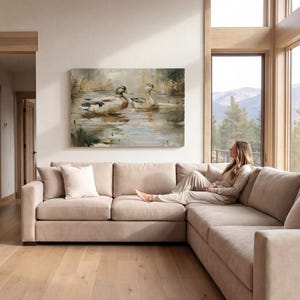 A woman sits on a beige sectional sofa in a spacious living room, gazing out a large window overlooking a scenic mountain landscape.