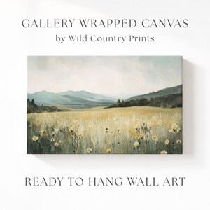 Puede incluir: Un lienzo envuelto en galería de Wild Country Prints con una pintura de paisaje de un prado con flores silvestres amarillas, hierbas verdes y montañas azules distantes bajo un cielo suave. El texto dice GALLERY WRAPPED CANVAS y READY TO HANG WALL ART.
