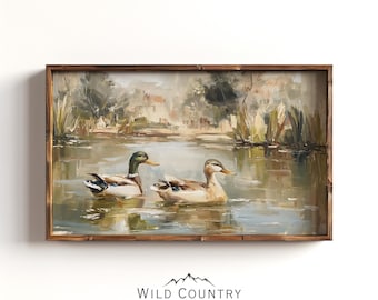 May include: Oil painting of two ducks swimming in a pond. The ducks have brown, white, and green feathers. The painting is in a wooden frame. The background shows a blurry landscape with trees and water. The Wild Country Collective logo is at the bottom.