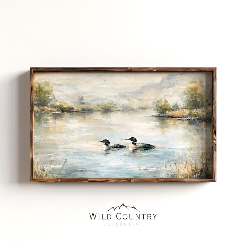 The image is a framed painting depicting two loon birds swimming in a lake, surrounded by a serene landscape with trees and mountains in the background.