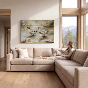 A woman sits on a beige sectional sofa in a spacious living room, gazing out a large window overlooking a scenic mountain landscape.