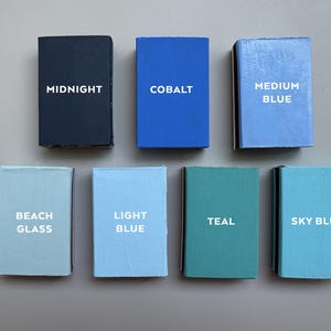 以下が含まれることがあります： 異なる青色の色合いの小さな塗料サンプルボックスが8つあります。ボックスには、次の色が表示されています。ミッドナイト、コバルト、ミディアムブルー、ビーチグラス、ライトブルー、ティール、スカイブルー