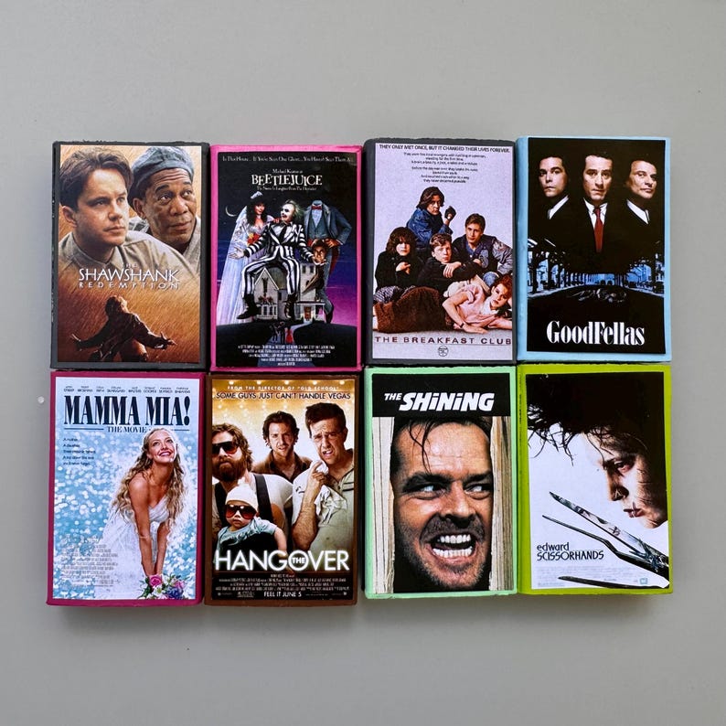 May include: A collection of eight VHS tapes featuring movie titles like "Shawshank Redemption," "Beetlejuice," "The Breakfast Club," and "Goodfellas." Each tape has a colorful cover with movie art and titles.