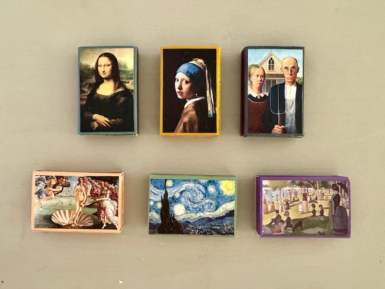 以下が含まれることがあります： 有名な絵画の小さな額装されたプリントが6つ。プリントはすべて異なる色とスタイルです。プリントはすべて明るい灰色の表面に一列に並んでいます。