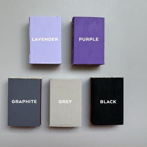 May include: Five small, rectangular boxes in shades of lavender, purple, graphite, grey, and black. Each box has a different color and the name of the color printed in white on the front.