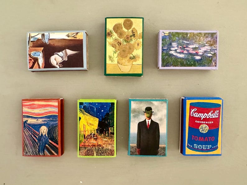 以下が含まれることがあります： 7つのマッチ箱のセットで、それぞれ異なる有名な絵画が描かれています。マッチ箱はすべて同じサイズと形をしていて、一列に並んでいます。絵画には、「叫び」、「星月夜」、「睡蓮」、「キャンベルスープ缶」、「人子の像」、そして他の2つが含まれています。
