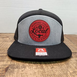 May include: A black and grey trucker hat with a red patch that says "Support Your Local Mechanic". The patch features a wrench and a tyre.