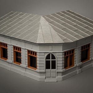 May include: A miniature architectural model of a corner building with a gray tiled roof and light gray walls. The windows have orange frames. The building has a front door and arched windows.