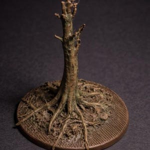 Op de afbeelding: Een gedetailleerde miniatuur boomsculptuur met zichtbare wortels en een getextureerde stam. De boom is bruin met groene accenten, geplaatst op een cirkelvormige basis. De basis heeft een getextureerd, geribbeld patroon.