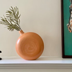 Sienna ceramics vase with a beautiful green leaf and half of a painting on a fireplace.