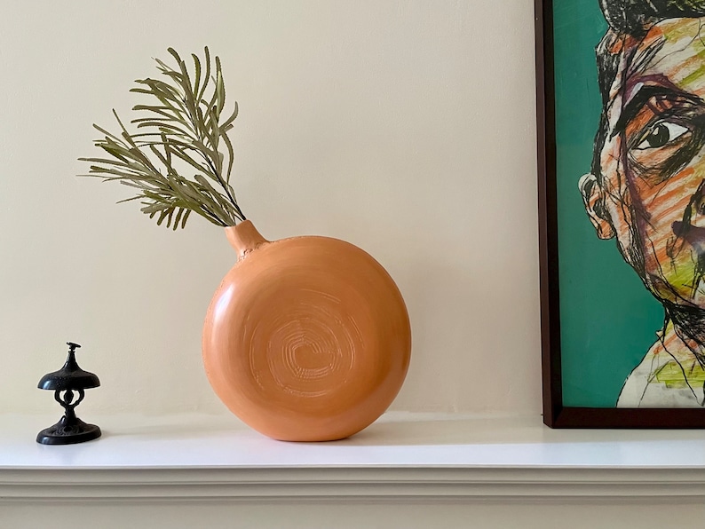 Sienna ceramics vase with a beautiful green leaf and half of a painting on a fireplace.