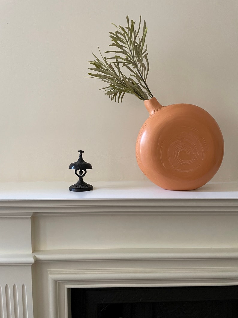 FACE of Sienna ceramic vase with a beautiful green leaf on a fireplace.