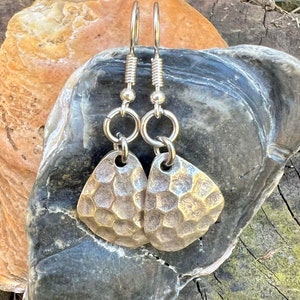 May include: A pair of silver earrings with a hammered metal design. The earrings are teardrop shaped and have a textured surface.
