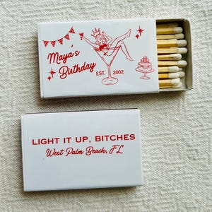 May include: Two white matchboxes with red text and illustrations. One box reads "Maya's Birthday" with a martini glass illustration. The other box reads "LIGHT IT UP, BITCHES" and "West Palm Beach, FL".
