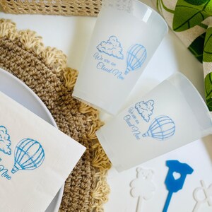 Op de afbeelding: Twee witte bekers met blauwe tekst en illustraties van wolken en luchtballonnen. De tekst op de bekers luidt "We are on Cloud Nine".