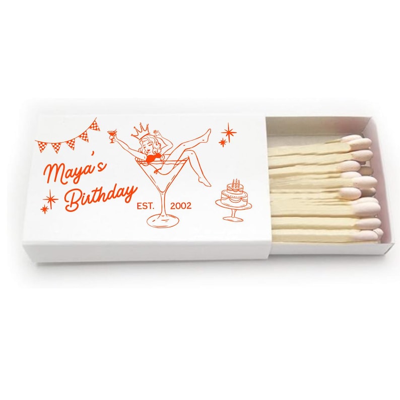 May include: A white matchbox with a red illustration of a woman in a martini glass, a cake, and the text "Maya's Birthday EST. 2002". The matchbox is open, revealing a row of matches with white tips.