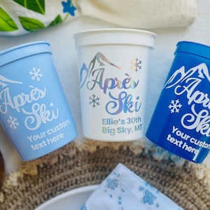 Puede incluir: Tres vasos de plástico azul y blanco con el texto "Apres Ski" en letras blancas. Un vaso tiene el texto "Ellie's 30th Big Sky, MT".
