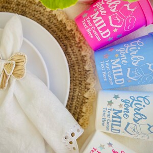 May include: A table setting featuring white plates, a white napkin with a woven bow napkin ring, and three plastic cups. The cups are pink, blue, and white, with the text "Girls gone Mild" and "Your Custom Text Here".