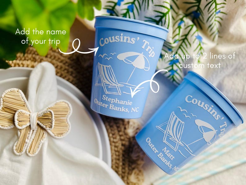 May include: Two light blue plastic cups with white text and beach-themed graphics. The cups read "Cousins' Trip" and include a beach chair, umbrella, and custom text. One cup says "Stephanie Outer Banks, NC" and the other says "Matt Outer Banks, NC".