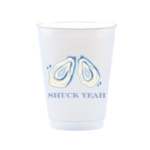 May include: A white plastic cup with a blue and cream oyster design and the text "SHUCK YEAH". The cup has a slightly frosted appearance and is suitable for cold beverages. The design includes two oysters and star accents.