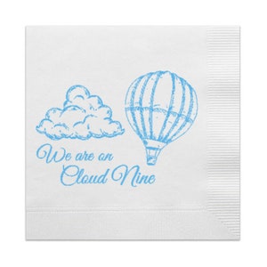 Op de afbeelding: Wit papieren servet met een blauwe illustratie van een luchtballon en een wolk. De tekst "We are on Cloud Nine" is onder de illustratie gedrukt.