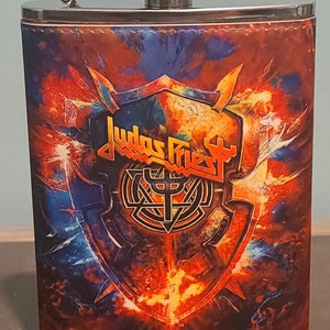 May include: A silver metal flask with a black and red design featuring the band Judas Priest and the words "Invincible Shield".