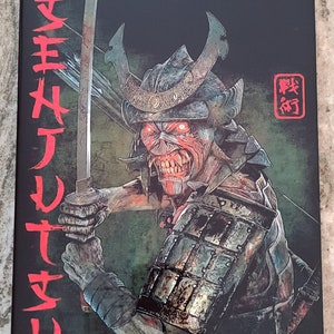 May include: A black and red Iron Maiden album cover featuring a samurai warrior with glowing red eyes. The warrior is holding a sword and wearing traditional armor. The text "IRON MAIDEN" is written in red letters at the top of the cover. The text "戦術" is written in red letters in a square in the upper right corner of the cover.
