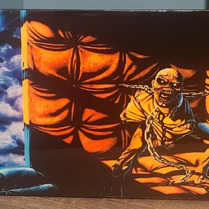 May include: A black and orange album cover with a metal head screaming and chained to a padded wall. The background is a dark blue sky with a bright moon.