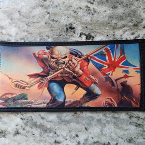 May include: A rectangular neoprene sleeve featuring a graphic illustration of a skeletal figure in a red military uniform holding a tattered British flag and a sword. The design includes a dark background with a silhouette of a grim reaper figure.