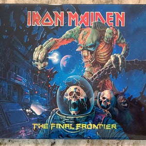 May include: A blue and black album cover with a green and red monster holding a chain. The monster is in front of a building and a planet. The text "IRON MAIDEN" is at the top of the cover and "THE FINAL FRONTIER" is at the bottom.