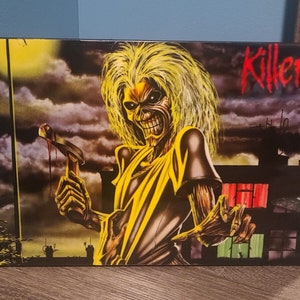 May include: A yellow and black album cover with a skull-like figure holding a bloody hammer. The album title "Killers" is in red letters.