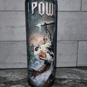 May include: A cylindrical tumbler with a detailed fantasy art design. The artwork features a warrior's arm, a chained weapon, and a winged creature. The word "POWER" is displayed at the top. The tumbler is designed to hold beverages.