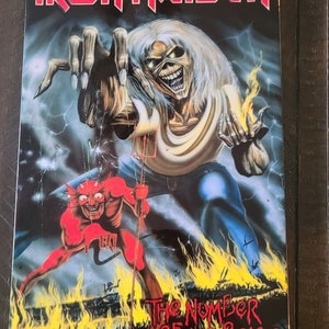 May include: A black and red album cover with the band name "IRON MAIDEN" in red letters. The cover features a white-haired man with a red devil figure in front of him. The album title "The Number of the Beast" is written in red letters at the bottom of the cover.