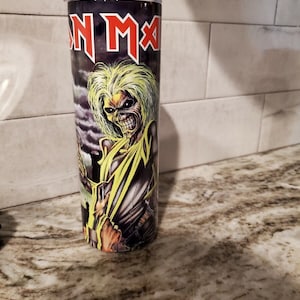 May include: A stainless steel tumbler with a black and yellow image of a metal band mascot. The image includes the text "Iron Maiden".