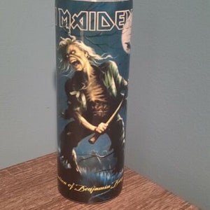 May include: A blue and black stainless steel tumbler with a graphic of a man holding a sword. The graphic is of the band Iron Maiden. The text "Iron Maiden" is printed on the tumbler.