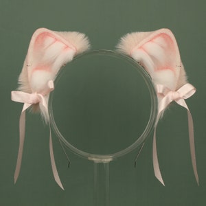 May include: A pair of pink furry cat ears with white tips and pink satin bows attached to a clear plastic headband.