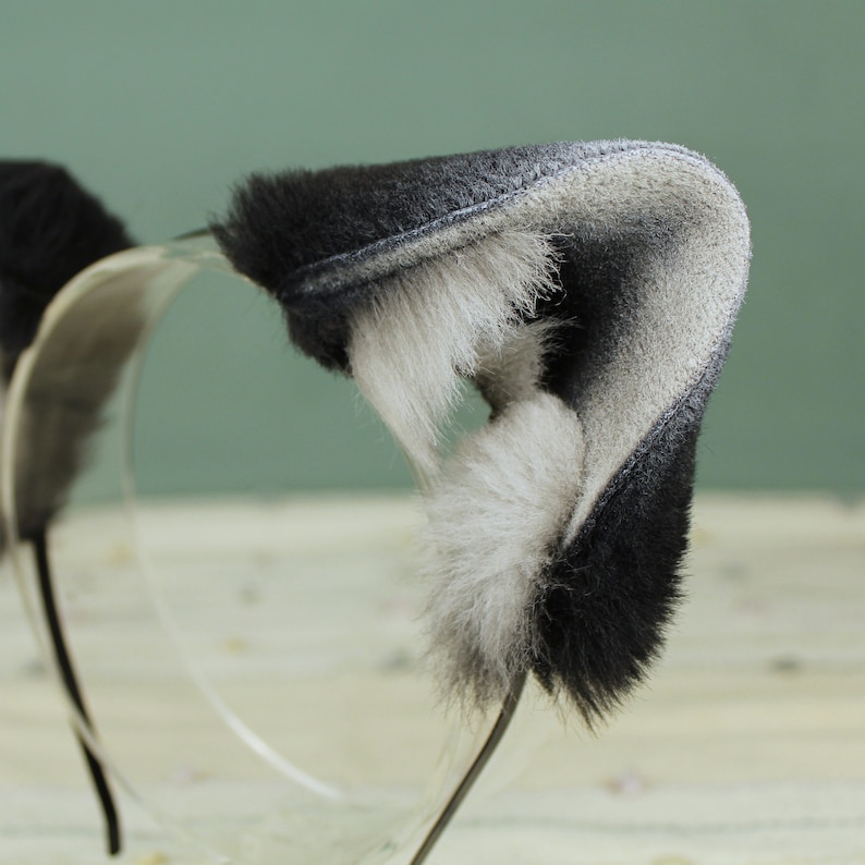 May include: A black and white furry headband with cat ears. The headband is made of soft, plush fabric and is perfect for adding a touch of whimsy to any outfit.