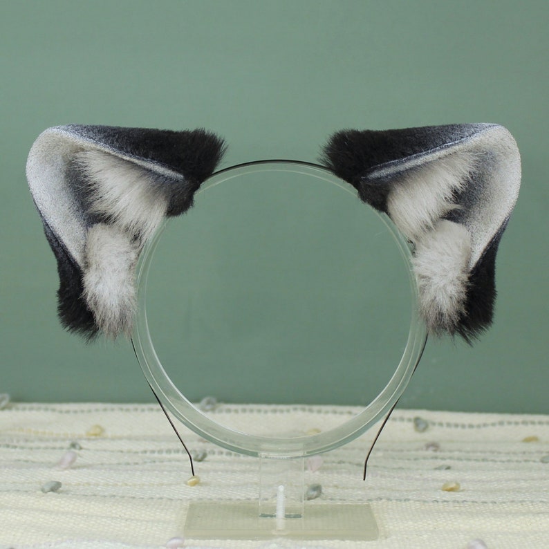 May include: A pair of black and white faux fur cat ears on a headband. The ears are soft and fluffy, with a black base and white tips.
